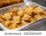 Chinese cream cheese wontons served in a silver catering container delivered for an event. Crispy crab rangoon