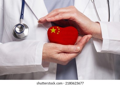 Chinese Doctor Holding Heart With Flag Of China Background. Healthcare, Charity, Insurance And Medicine Concept