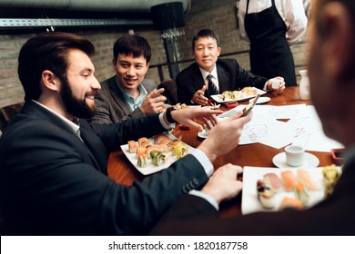 Chinese with European businessmen have lunch in a sushi bar. Businessmen are sitting in a restaurant and having lunch while working with papers.