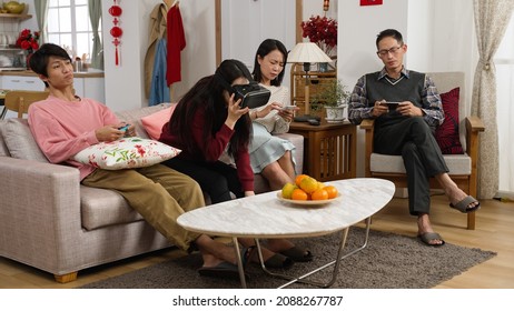 Chinese Family Feeling Bored And Neglecting Each Other While Playing With Phone. Virtual Reality Device And Video Game In The Living At Home During Chinese New Year Holiday