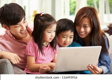 Chinese Family Using Laptop Whilst Relaxing On Sofa At Home