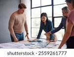 Chinese female architect discussing with multiethnic team while examining architectural plans and materials during a meeting. Casual architects and engineers discussing about building construction.