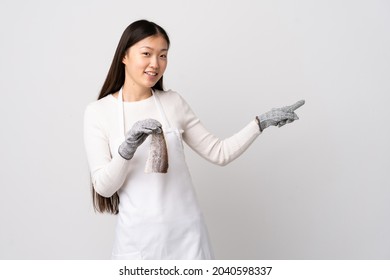 Chinese fishmonger wearing an apron and holding a raw fish over isolated white background pointing finger to the side and presenting a product