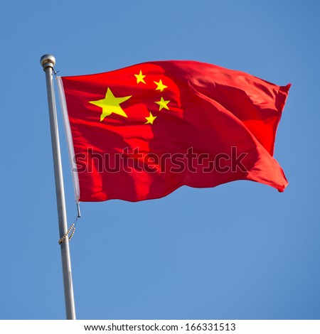 Chinese flag with flag pole waving in the wind over blue sky background.