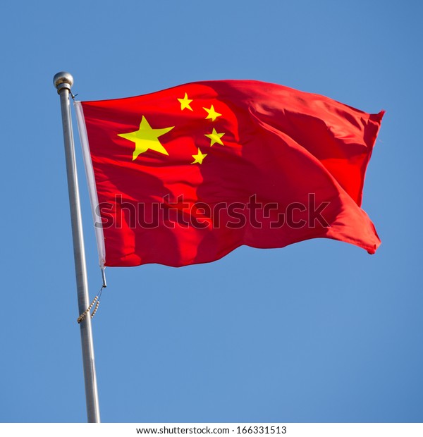 Chinese flag with flag pole waving in the\
wind over blue sky\
background.