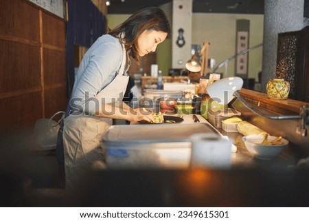 Chinese food, chef and an asian woman in a sushi restaurant to serve a traditional meal for nutrition. Kitchen, cooking or preparation with a happy young employee in an eatery for fine dining cuisine