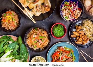 Chinese Food On Dark Wooden Table. Noodles, Fried Rice, Dumplings, Stir Fry Chicken, Dim Sum, Spring Rolls, Bean Sprouts, Bok Choy. Chinese Cuisine Set. Dinner Party. Top View. Chinese Restaurant