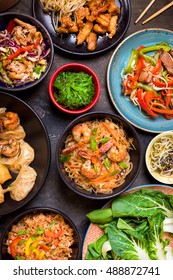 Chinese Food On Dark Wooden Table. Noodles, Fried Rice, Dumplings, Stir Fry Chicken, Dim Sum, Spring Rolls, Bean Sprouts, Bok Choy. Chinese Cuisine Set. Dinner Party. Top View. Chinese Restaurant