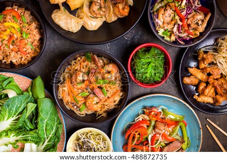 Chinese food on dark wooden table. Noodles, fried rice, dumplings, stir fry chicken, dim sum, spring rolls, bean sprouts, bok choy. Chinese cuisine set. Dinner party. Top view. Chinese restaurant