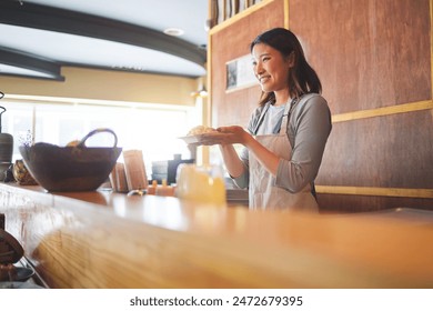 Chinese food, waitress and an asian woman in a sushi restaurant to serve a traditional meal for nutrition. Kitchen, smile and cooking with a happy young employee in an eatery for fine dining cuisine - Powered by Shutterstock