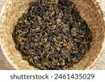 Chinese Gunpowder tea leaves rolled into a small pellets, in rustic dish on burlap close up top view