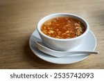 Chinese hot and sour soup with wispy beaten eggs, meat and vegetables in a chicken stock, white bowl with a porcelain spoon on a wooden table in an Asian restaurant, copy space, selected focus