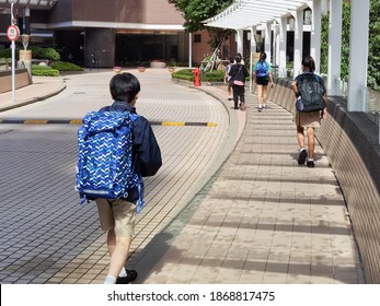 Chinese and Indian Boy and girls of international elementary- primary school carrying heavy big school bags  return home or go to school, walking along street in Hong Kong on sunny day