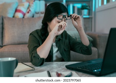 chinese lady sitting at table is getting fatigued eye from gazing at pc screen without resting. asian female removing her glasses and rubbing her eye to ease the pain. health and eye care concept - Shutterstock ID 2023797065