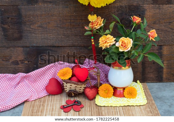 A\
Chinese lantern hangs over the table. There are yellow roses in a\
vase on the table. Nearby are calendula flowers, hearts and a key.\
A wicker car with scarlet hearts stands on the\
side.\
