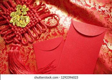 Chinese Lunar New Year celebrations theme blank red envelope and hanging decoration with golden blessing word means ‘good fortune’ on red and gold traditional Chinese pattern brocade fabric background