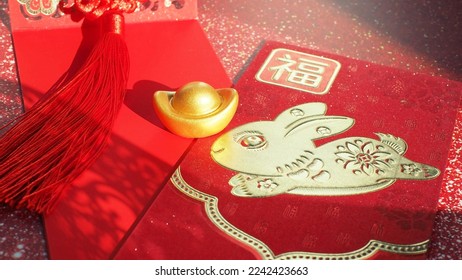 Chinese Lunar New Year red envelope with rabbit and blessing word contained money as a gift on red background with ancient gold bullion nugget. The Chinese word means ‘happiness and good fortune’. - Shutterstock ID 2242423663