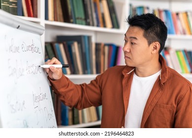 Chinese Male Tutor Writing On Whiteboard Having English Class Standing In Modern Classroom Indoors. Teacher Man Teaching Language Grammar Rules. School And College Education. Selective Focus