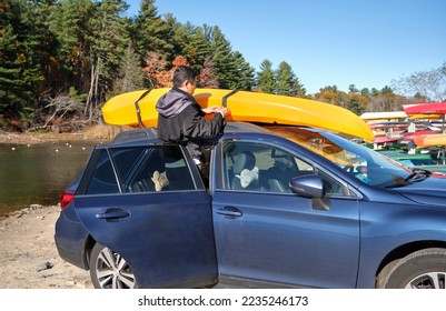 Chinese man in black jacket unloading yellow kayak off of blue car by a pond on sunny day - Powered by Shutterstock