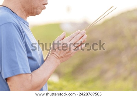 The Chinese man is holding joss stick for paying respect to ancestor on Qingming tomb stone in the Chinese Qingming ritual. Middle Aged Asian man hand respecting and blessing. Chinese faith ritual