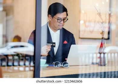 A Chinese man in a suit keys in his credit card payment information into his laptop to purchase something online in an ecommerce store. 
