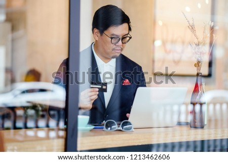 A Chinese man in a suit keys in his credit card payment information into his laptop to purchase something online in an ecommerce store. 