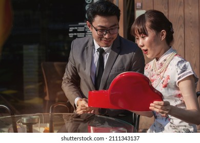 Chinese Man Surprise Gift Young Woman Girlfriend With Heart Shape Gift Box At Outdoor Coffee Shop, Happy Valentine's Day