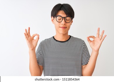 Chinese man wearing glasses and navy striped t-shirt standing over isolated white background relax and smiling with eyes closed doing meditation gesture with fingers. Yoga concept. - Powered by Shutterstock