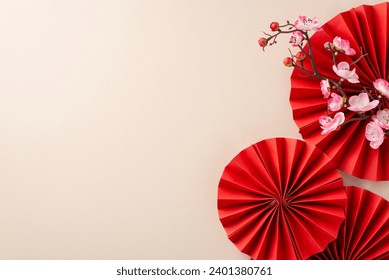 Chinese New Year décor arrangement. Top view of red paper fans, and sakura bloom on a festive pastel beige table with empty space for wishes