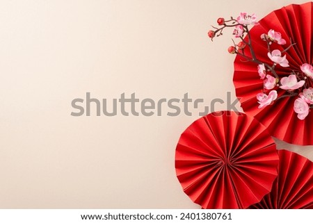 Chinese New Year décor arrangement. Top view of red paper fans, and sakura bloom on a festive pastel beige table with empty space for wishes