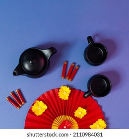 Chinese New Year Composition With Teapot, Teacups, Red Paper Fan And Firecrackers On Pastel Blue Background.