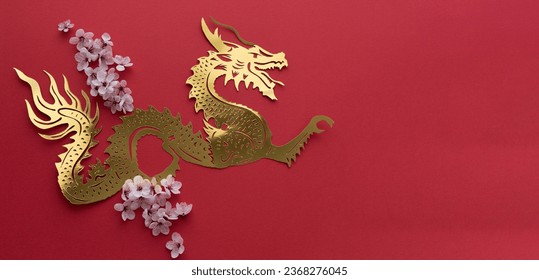Chinese New Year. Dragon cut out in gilt paper with plum blossom decoration on red background. Copy space. Top view.