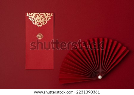 Chinese new year festival decoration over red background. traditional lunar new year red pockets, paper fan for fortune, prosperity, wealth. Flat lay, top view