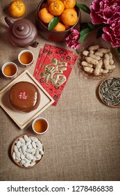 Chinese New Year Festival Food And Drink. Orange, Red Packet, New Year Cake, Peanuts, Sunflower Seed, Mealon Seed, Tea And Peony Flower On Table.Translation Of Text Appear In Image: Prosperity