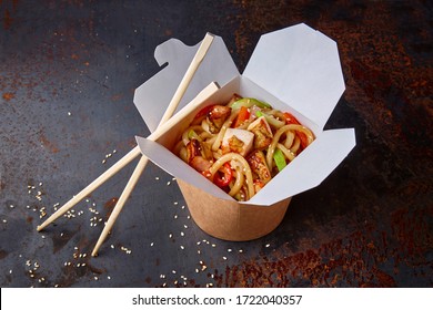 Chinese noodles with chicken and vegetables in a cardboard box on a dark background, Asian food delivery, concept of street food,  copy space