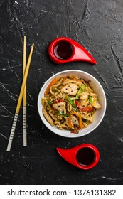 Chinese noodles in a Cup with chicken and vegetables with sticks. Wok food from the restaurant on a dark background from a top view. - Shutterstock ID 1376131382
