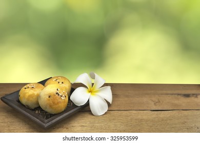 Chinese pastry and white flower on black dish over wooden table over blurry green background