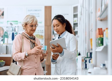 Chinese pharmacist using digital tablet while assisting her senior customer in buying medicine in a pharmacy. - Powered by Shutterstock