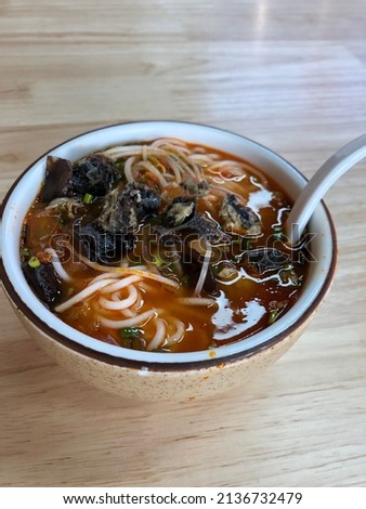 Chinese rice noodles in thick tomato broth with brewed black chicken and wood ear on the top and spring sprouts at the bottom.