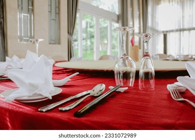 Chinese set table equipment arrange on red cover round table with lazy susan, setting up with white chinaware and napkin, silverware spoon, fork and knife, black chopsticks, wine glasses.