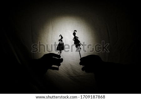 Chinese shadow theater for children projected on a bed sheet, themed of Saint George. The shadows are of cardboard, you can see the hand that manipulates them. dragon, tales, storyteller, princess
