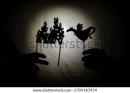 Chinese shadow theater for children projected on a bed sheet, themed of Saint George. The shadows are of cardboard, you can see the hand that manipulates them. dragon, tales, storyteller, castle