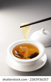 Chinese Shark's Fin Soup with brown sauce serve in Royal yellow bowl, decoration with bean sprouts and Coriander, on grey wooden background.