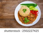 Chinese style chicken gravy fragrant with sesame oil and steamed jasmine brown rice with side dishes of scallions, cucumber, cilantro, red chilli in white plate on wooden table.