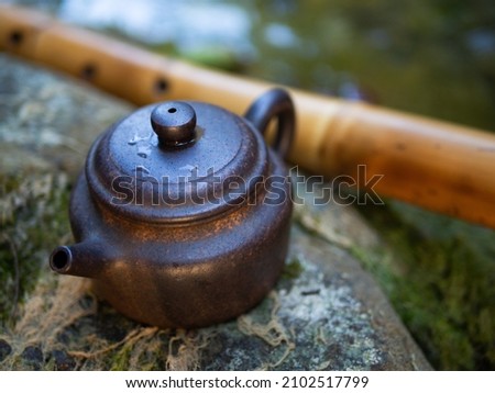 For the Chinese tea ceremony. Small brown clay teapot. Standing on a large gray stone. Against the backdrop of nature and green moss. Behind is a bamboo flute.