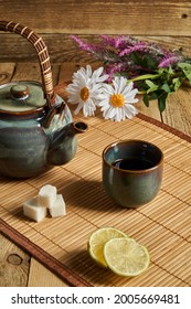 Chinese Tea Party. A Ceramic Teapot And Fancy Colored Teacup Sit On A Mat Next To Sugar, Limes And Flowers