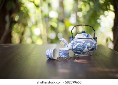 Chinese teapot and tea cups with dried tea leaf on dark brown table in green garden / Selective focus 