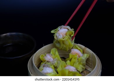 Chinese Traditional Brunch, Dim Sum, Red Chopsticks Holding Green Dumpling , Shumai, In Bamboo Basket