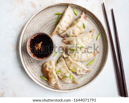 Chinese traditional dumplings - gyoza with pork and vegetables on a rustic plate with soy sauce in a bowl. Top view.
