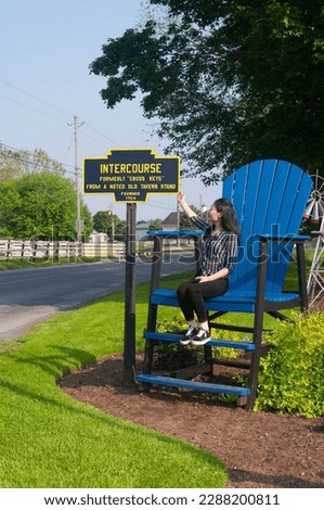 A chinese woman looking at the intercourse pennsylvania sign while sitting in a large blue chair.